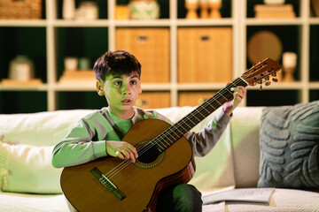 Obraz premium Young boy learning to play classical acoustic guitar at home