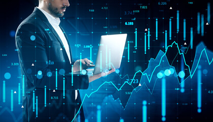Businessman analyzing forex and financial market data on laptop with digital stock charts and currency graphs on blue background concept.