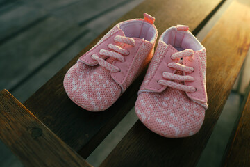 Close-up of a pair of pink baby shoes placed on a wooden bench, photographed in warm natural light.