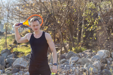 Man posing with colorful racket behind head outdoors