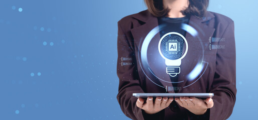 Woman holding tablet with glowing AI chip and bulb concept hologram on blue tech background.