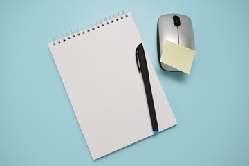 Blank notebook with pen and wireless mouse on blue background