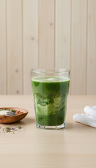Refreshing Green Smoothie in Tall Glass with Wooden Bowl of Seeds and Grains on a Table with Wood Paneled Background and Soft Lighting