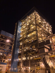 Towering industrial power plant illuminated against the dark night sky, showcasing complex...