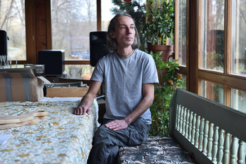 Man with long hair sitting in a sunroom looking out the window