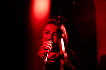 Female singer in red light performing passionately on stage at live concert