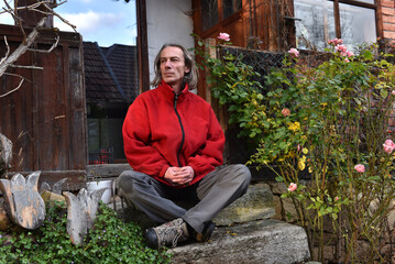 Handsome man with long hair sitting on a stone step in a rustic garden