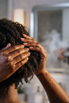 Back view of a Black woman performing a wash day routine on natural afro hair, massaging scalp with shampoo or conditioner, symbolizing self care and beauty rituals