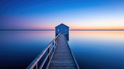 Fototapeta premium A blue building on water with a wooden walkway leading to it under a gradient sky at dusk or dawn