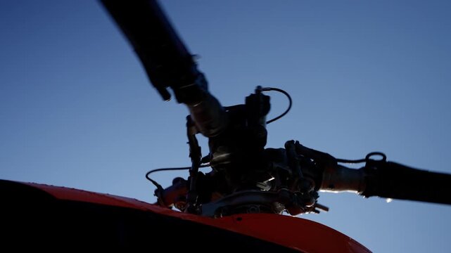 Close-up view of a helicopter rotor hub and swashplate assembly with blades silhouetted against a blue sky, emphasizing mechanical detail and precision in aviation engineering