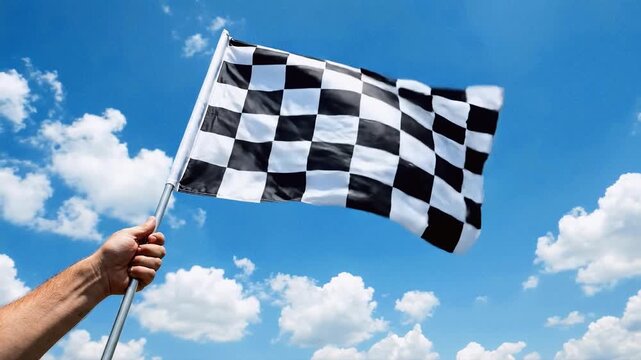 Checkered racing flag waving in the wind against a blue sky with clouds. Hand holding a finish line signal for motorsport victory