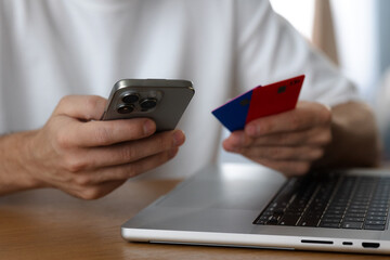 Man holds smartphone and credit cards next to laptop close-up