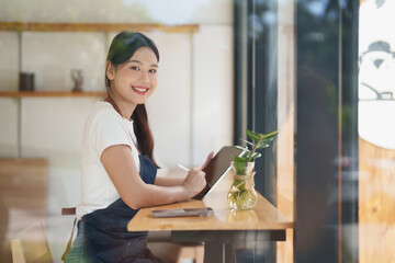Asian woman barista working with tablet in coffee shop