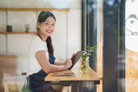Asian woman barista working with tablet in coffee shop - Powered by Adobe
