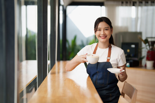 Asian woman barista smiling offering hot coffee at cafe