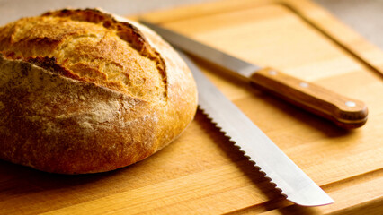 Loaf of bread on cutting board with knife.