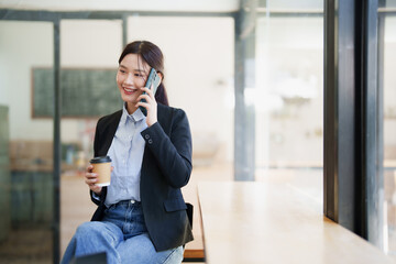 Young businesswoman talking on smartphone holding coffee