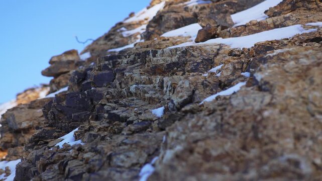 Detailed rocky hillside appears closer showing fractured mineral layers covered with snow. Atmosphere becomes crisp and powerfully alpine