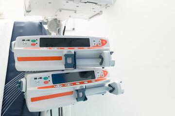 Modern electronic syringe pumps seen by a hospital bed in a typical critical care and emergency room within a British hospital. The bed can be seen on the left.