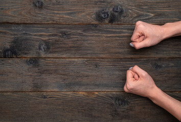 Female hands clenched into fists on rustic wooden background, showing raw strength and determination. Woman's fists resting firmly on wooden table, conveying firm resolve and emotional strength.