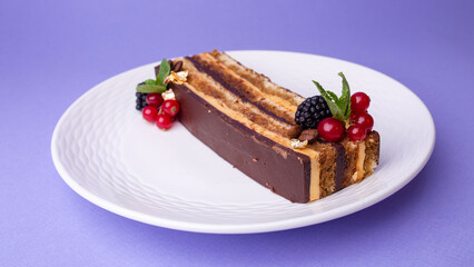 Slice of chocolate cake with berries on white plate against purple background