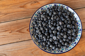 Fresh, raw blue huckleberry berries (Vaccinium corymbosum) on a platter. Rustic wooden background with copy space.  
