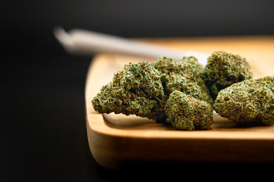 Cannabis buds presentation, cannabis flower presentation and the finished joint, pre-roll in the background elegant on a wooden rolling tray professional product photo