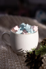 side mug overflowing with pastel marshmallows by knitted blanket. warm directional light creates cozy glow