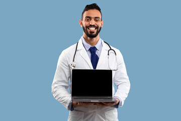 A doctor stands confidently with a broad smile, holding a laptop in front of him. He wears a white coat and a stethoscope around his neck.