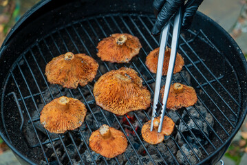 A person uses tongs to flip grilled mushrooms sizzling on a charcoal barbecue
