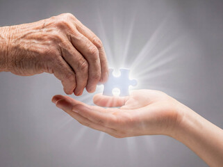 Old hand giving glowing puzzle piece to young hand solution concept problem solving connection logic game missing part success teamwork magic light abstract background closeup