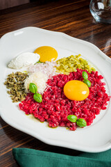 A vibrant plate showcases raw meat mixed with egg yolks and garnished with herbs and pickles