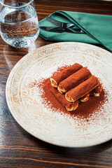 Layers of rich tiramisu dusted with cocoa powder are beautifully arranged on a decorative plate