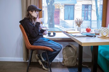 Young woman reading a book in a cozy cafe with a cup of cocoa.