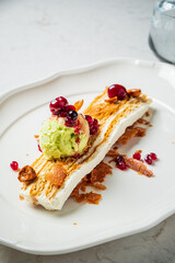 Decadent dessert on a white plate with ice cream, berries, and crispy layers