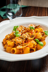 A vibrant dish of rigatoni pasta mixed with shellfish and garnished with fresh basil sits elegantly