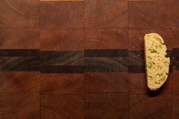 Single, homemade pistachio and orange biscotti on a wood end grain cutting board with copy space