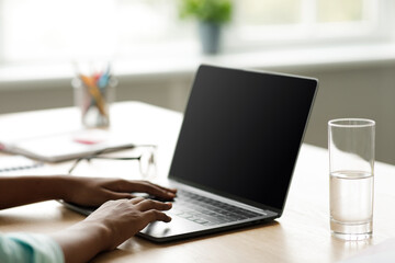 A teenage African American girl types on her laptop while studying at home.
