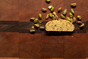 Twice baked biscotti cookie on an end grain cutting board, surrounded by pistachio nuts and crumbs with copy space