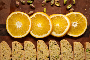 Fresh orange slices, homemade biscotti cookies, and pistachio nuts arranged on a wood cutting board