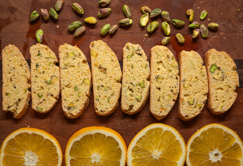 Cozy holiday baking - orange and pistachio biscotti cookies, sliced and presented with pistachio nuts and orange slices