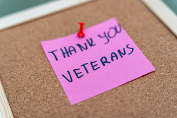 A handwritten note on a pink sticky paper saying thank you veterans. This message expresses gratitude and respect, suitable for commemorative or patriotic themes.