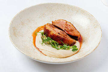 Tender slices of duck breast are artfully presented on a creamy puree, garnished with herbs