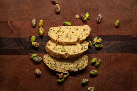 Three pistachio biscotti pastries arranged with pistachio nuts on a wood cutting board