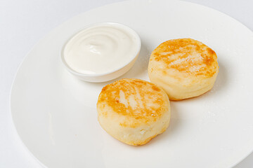 Two golden cheese pancakes sit beside a small bowl of creamy sour cream on a bright plate