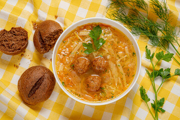 Delicious vegetable soup with tender meatballs served alongside fresh herbs and brown bread