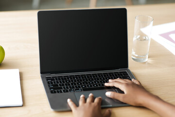 An adolescent girl types on a laptop with a blank screen while studying at home. She is focused on her studies in a safe and quiet interior setting, adapting to online learning during the pandemic.