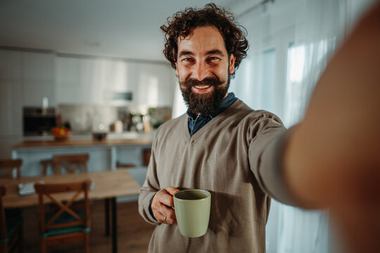 Smiling man taking selfie with coffee at home
