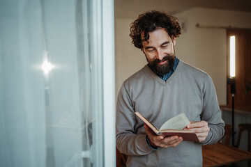 Fototapeta premium Bearded man reading old book feeling relaxed indoors