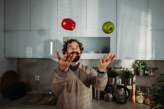 Man juggling red and green apples in kitchen - Powered by Adobe